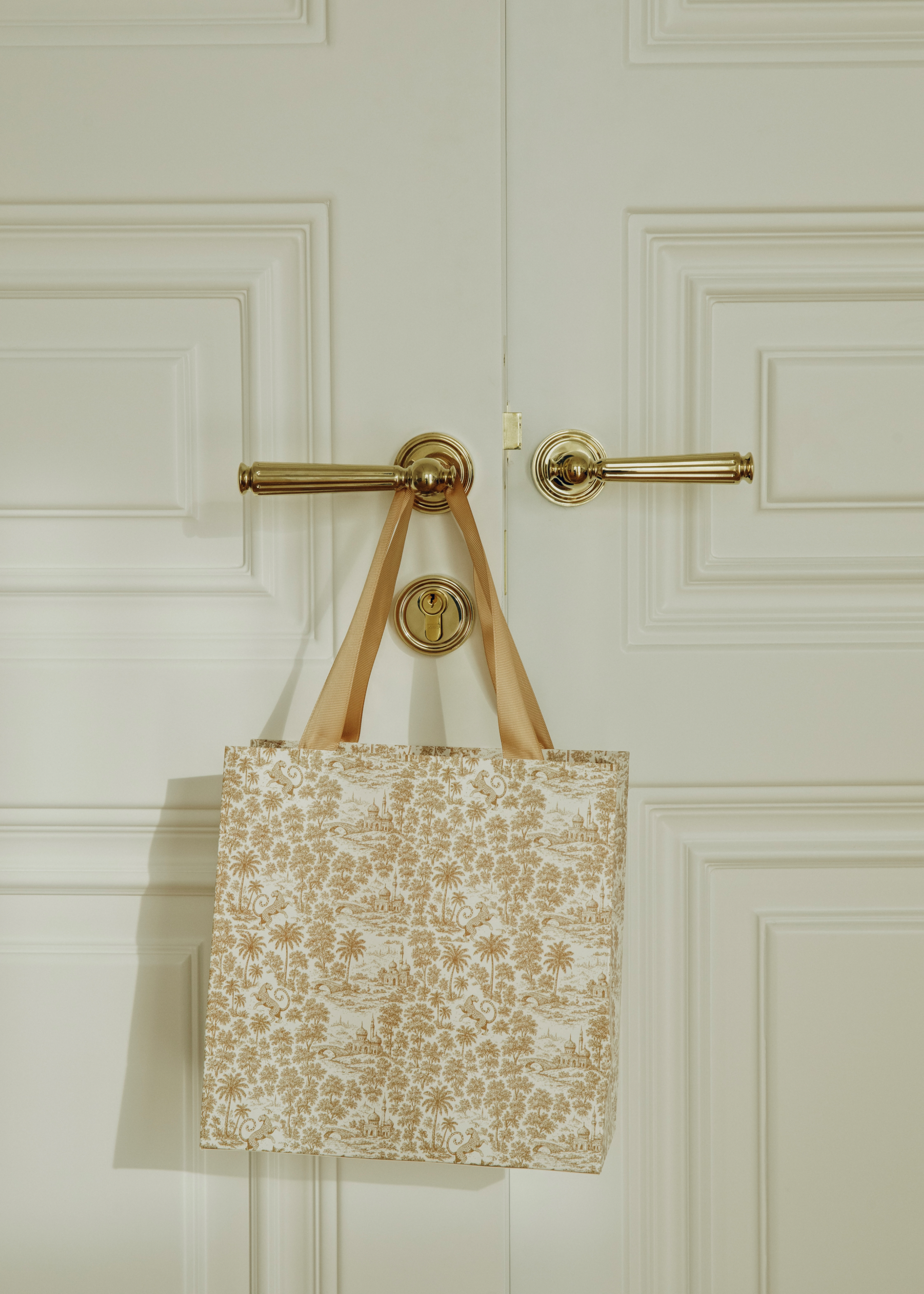 Floral-patterned tote bag hanging on a gold door handle against a white paneled door.
